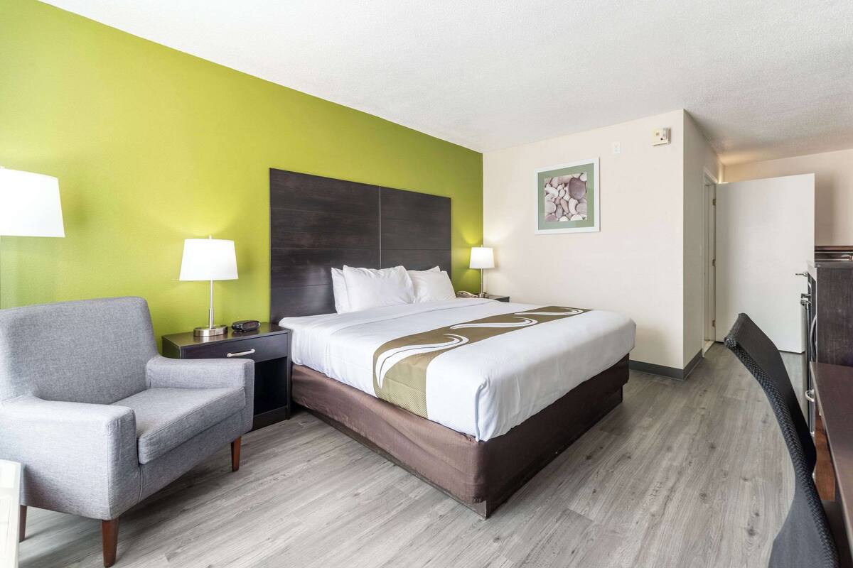 A hotel room with a bed, a chair, a nightstand, and a lamp.