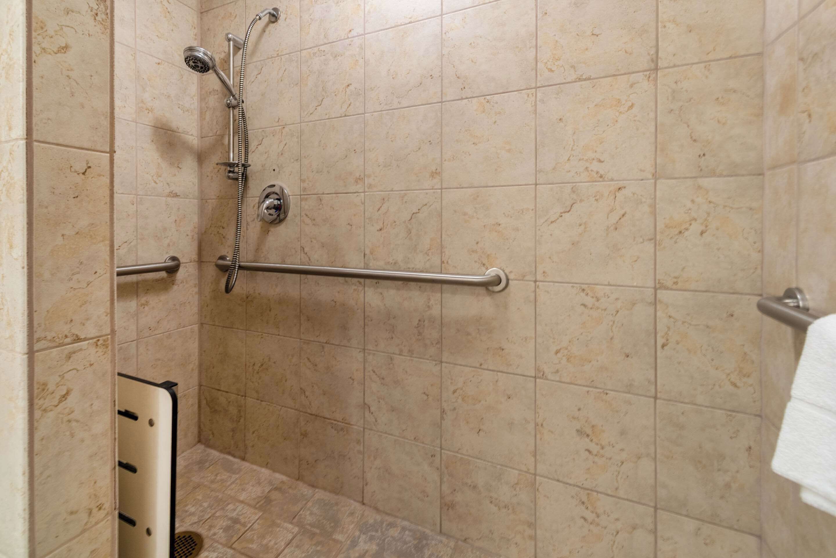 A shower area with a grab bar, a handheld showerhead, and a towel rack.