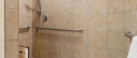 A shower area with a grab bar, a handheld showerhead, and a towel rack.