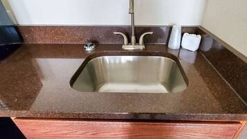 A kitchen sink with a faucet, a soap dispenser, and a glass container on a brown countertop.