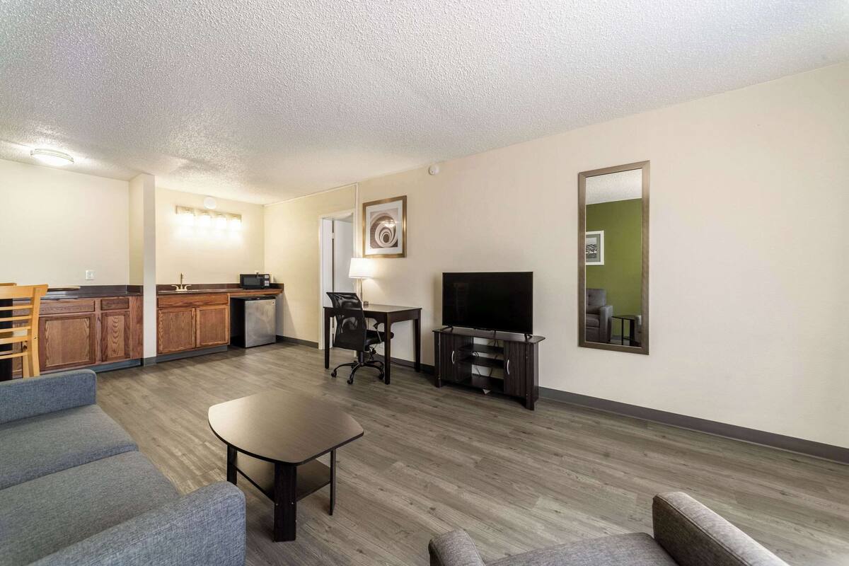 A modern living room with a sofa, a coffee table, a TV, and a kitchen area with wooden cabinets and a refrigerator.