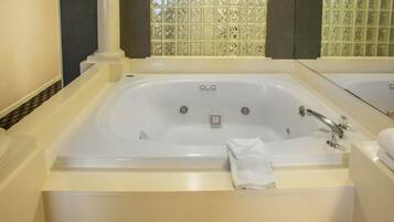 Una bañera grande y rectangular con un panel de control, una zona de ducha con cerramiento de vidrio y un espejo sobre la bañera.