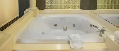 A large, rectangular bathtub with a control panel, a glass-enclosed shower area, and a mirror above the tub.