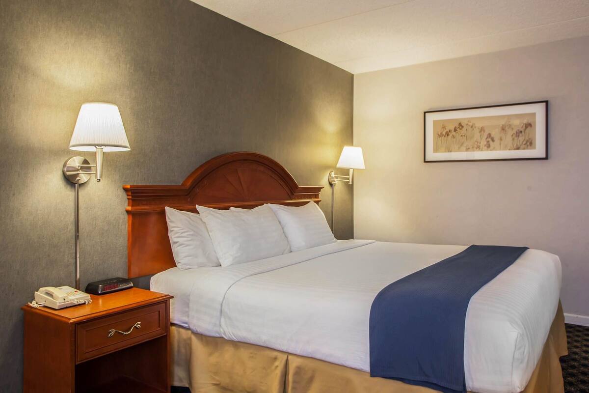 A hotel room with a large bed, two bedside lamps, a nightstand with a phone, and a framed picture on the wall.