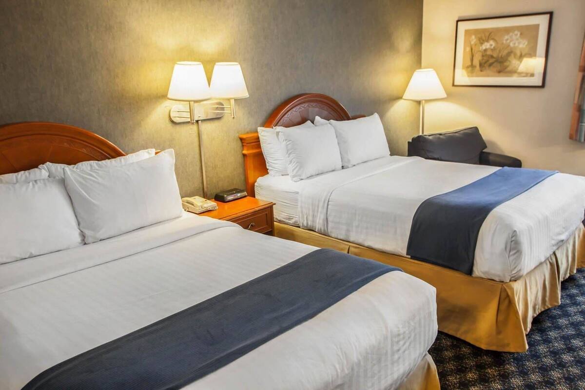 A hotel room with two beds, a nightstand, a lamp, and a framed picture on the wall.