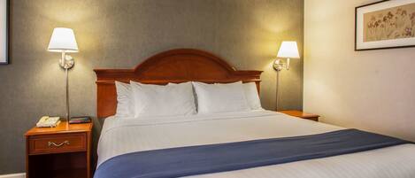 A hotel room with a large bed, two bedside tables, a nightstand, and two wall-mounted lamps.