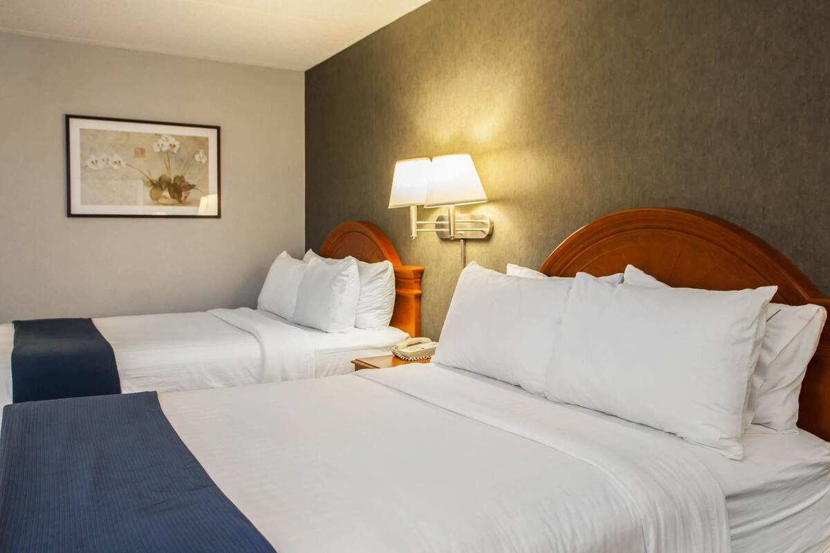 A hotel room with two beds, a bedside lamp, a framed picture on the wall, and a telephone on the nightstand.