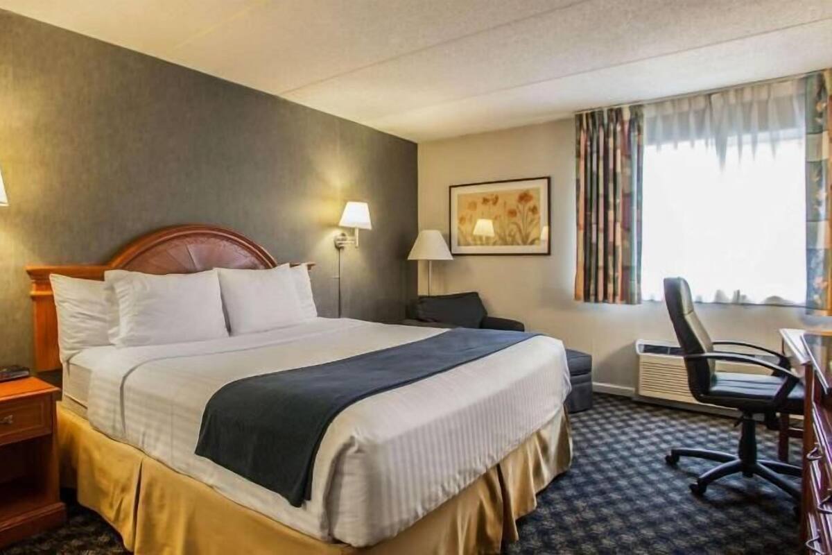 A hotel room with a bed, bedside lamps, a desk, a chair, and a window with curtains.