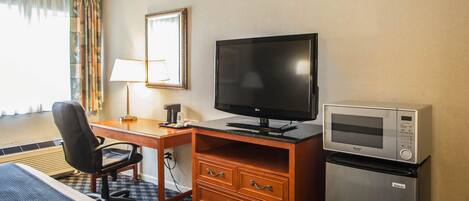 Une chambre d’hôtel équipée d’un lit, d’un bureau avec un ordinateur, d’une télévision, d’un four à micro-ondes et d’une commode.
