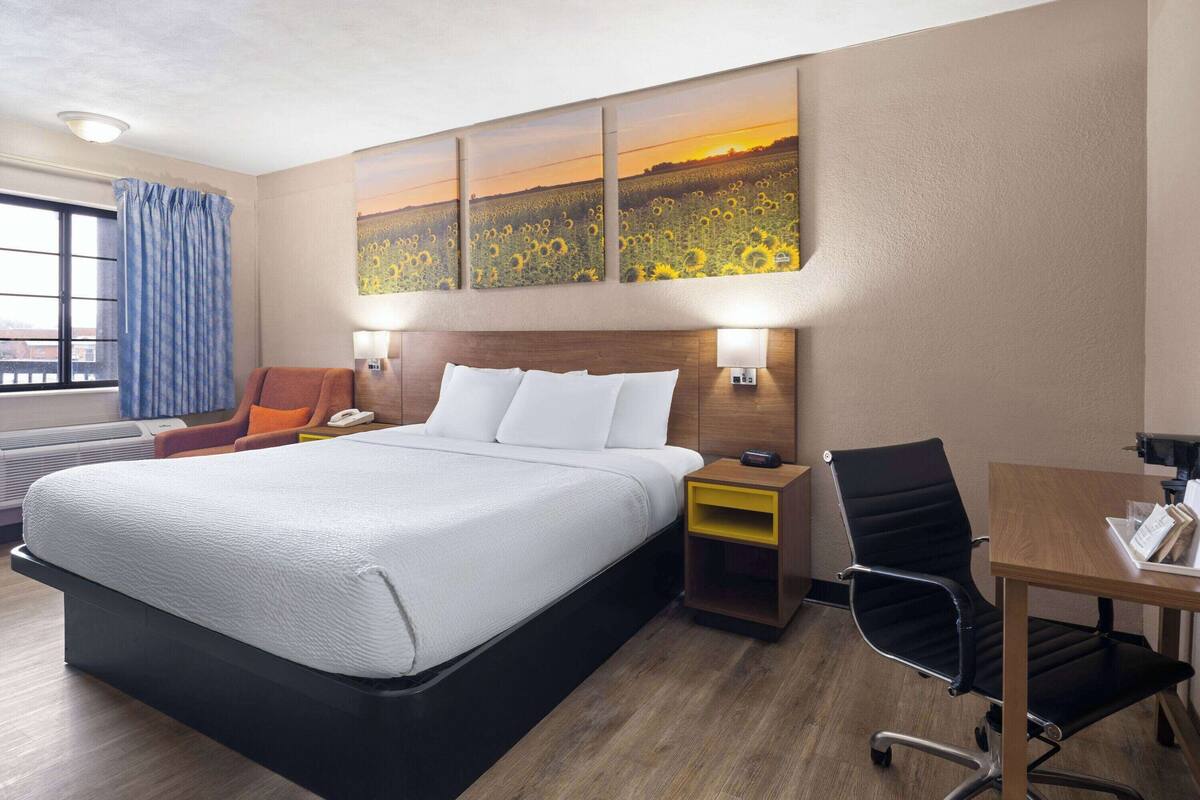 A hotel room with a large bed, a desk, a chair, a nightstand, and a wall-mounted artwork.