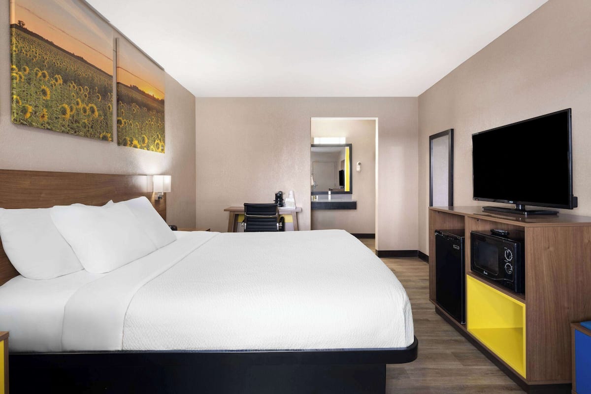A hotel room with a large bed, a TV, a desk with a chair, a microwave, and a small refrigerator.