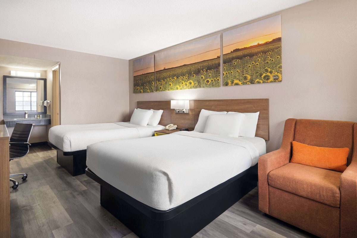 A hotel room with two beds, a desk, and a chair.
