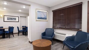 Ett hotellrum med en matplats, ett runt träbord, två blå stolar, en inramad tavla och ett fönster med persienner.