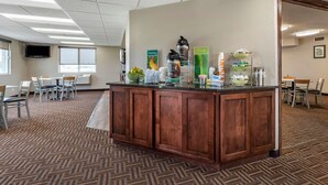 A hotel reception area with a wooden counter, a television mounted on the wall, and a buffet setup with various food items and drink dispensers. - Quality Inn Creston (Creston)