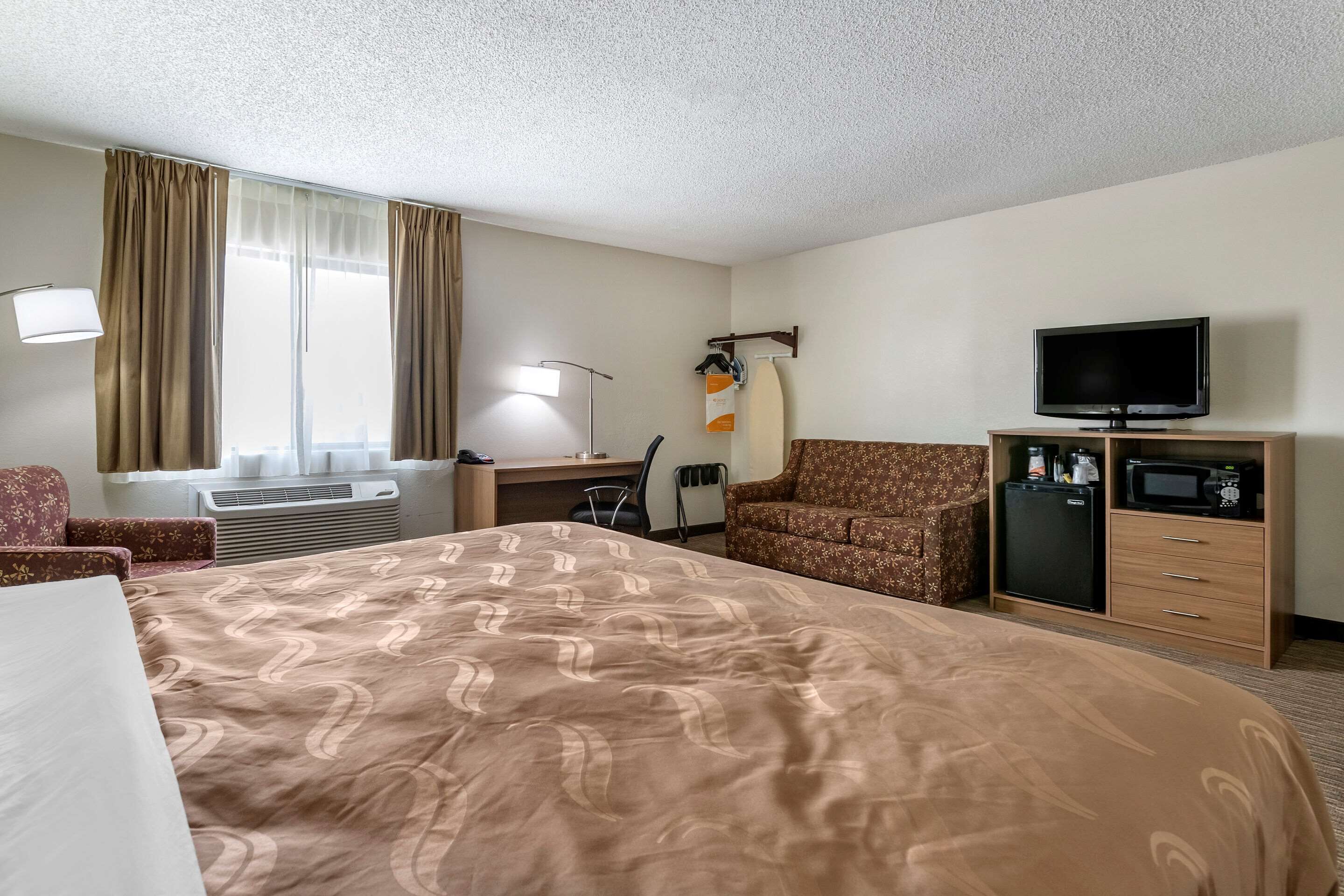 A hotel room with a large bed, a desk with a chair, a television, a microwave, and a wardrobe.