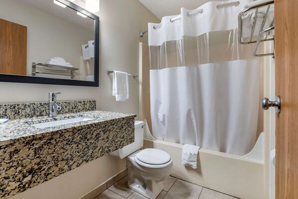 A bathroom with a granite countertop sink, a toilet, and a bathtub with a shower curtain.