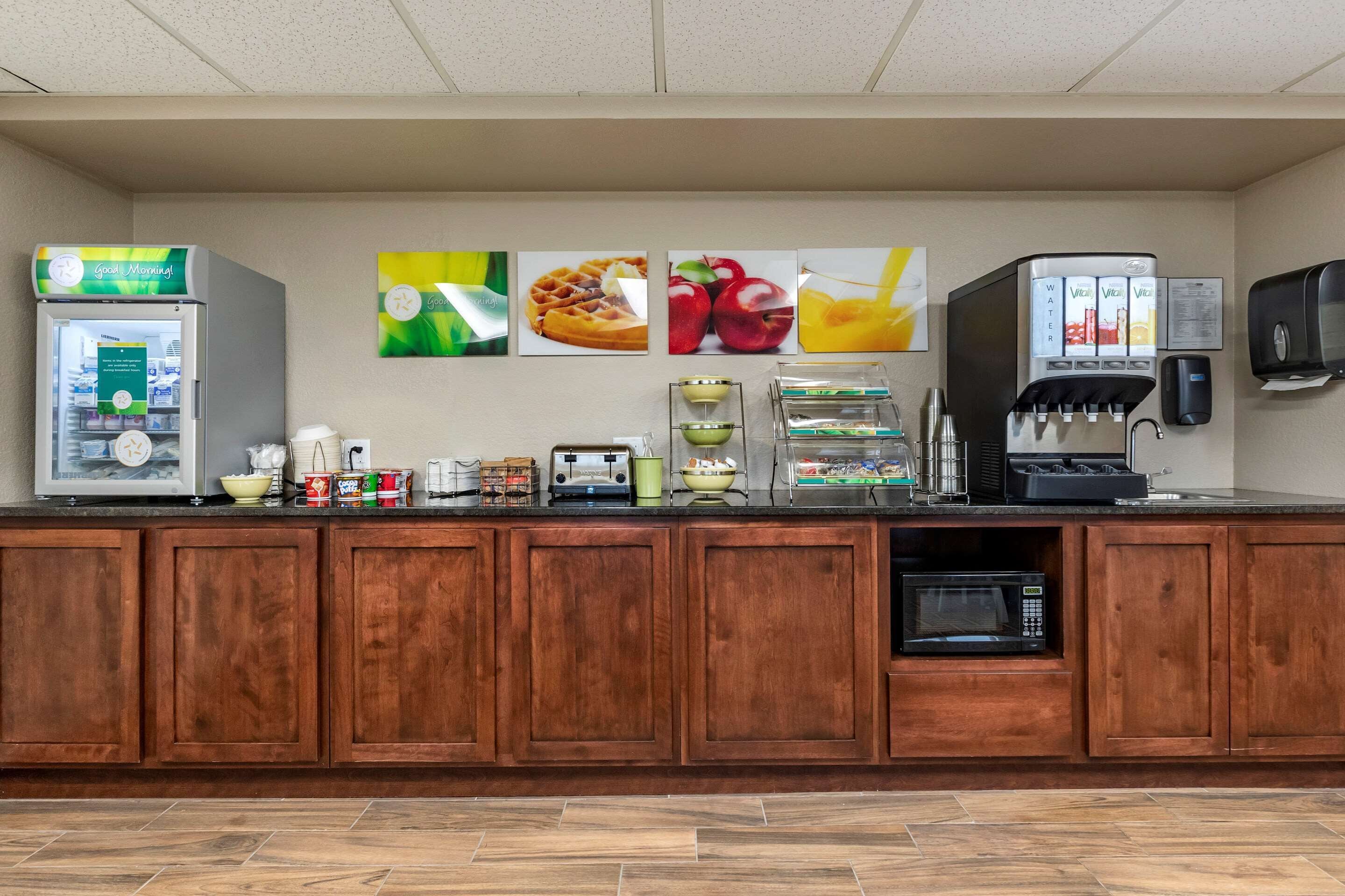 A hotel reception area with a refrigerator, coffee machine, microwave, and a beverage dispenser.