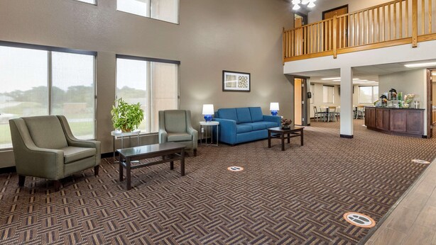 A spacious lobby with a high ceiling, a blue sofa, armchairs, and a coffee table. There is a reception desk and a staircase to an upper level. - Quality Inn Creston (Creston)
