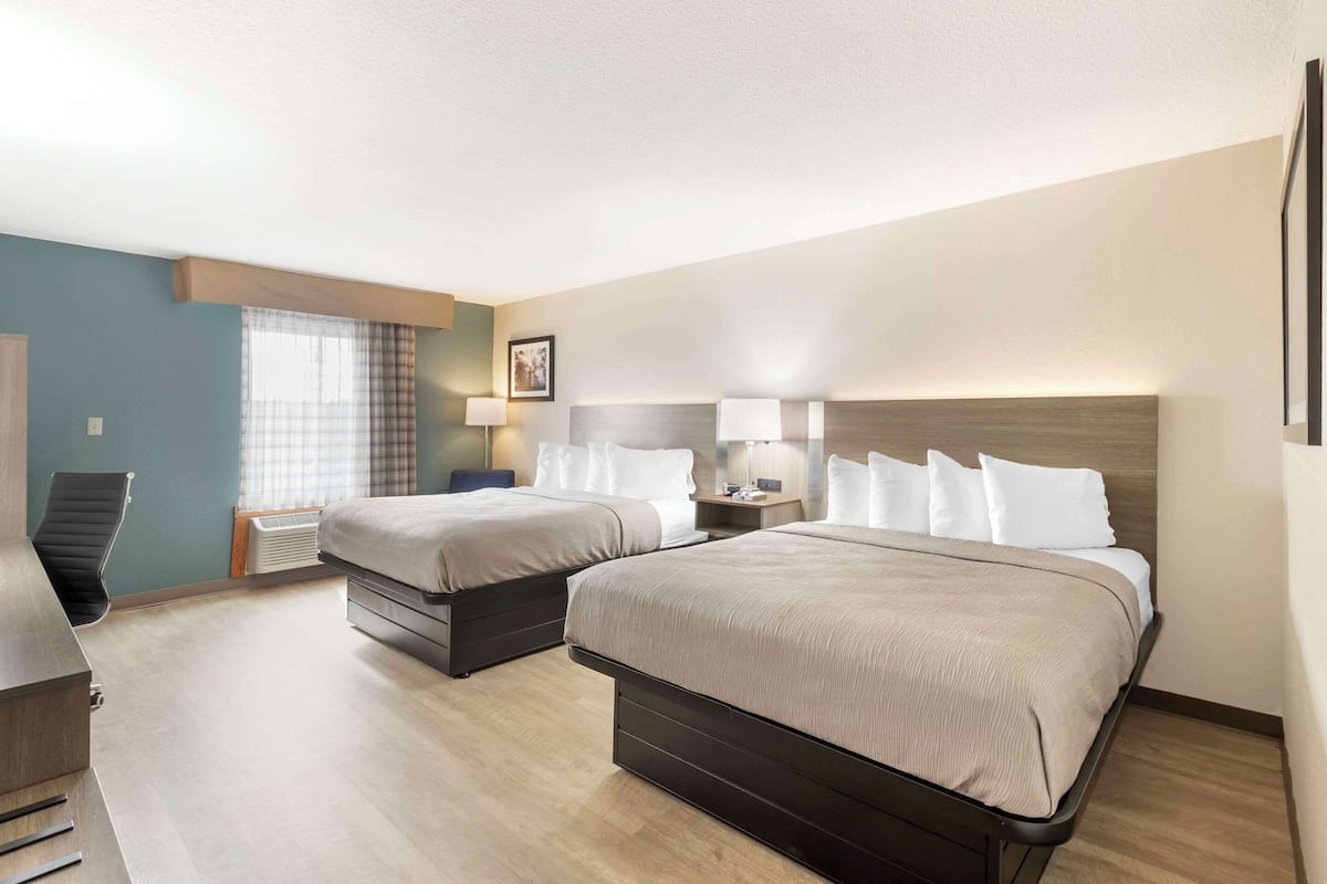 A hotel room with two beds, a desk, and a chair.