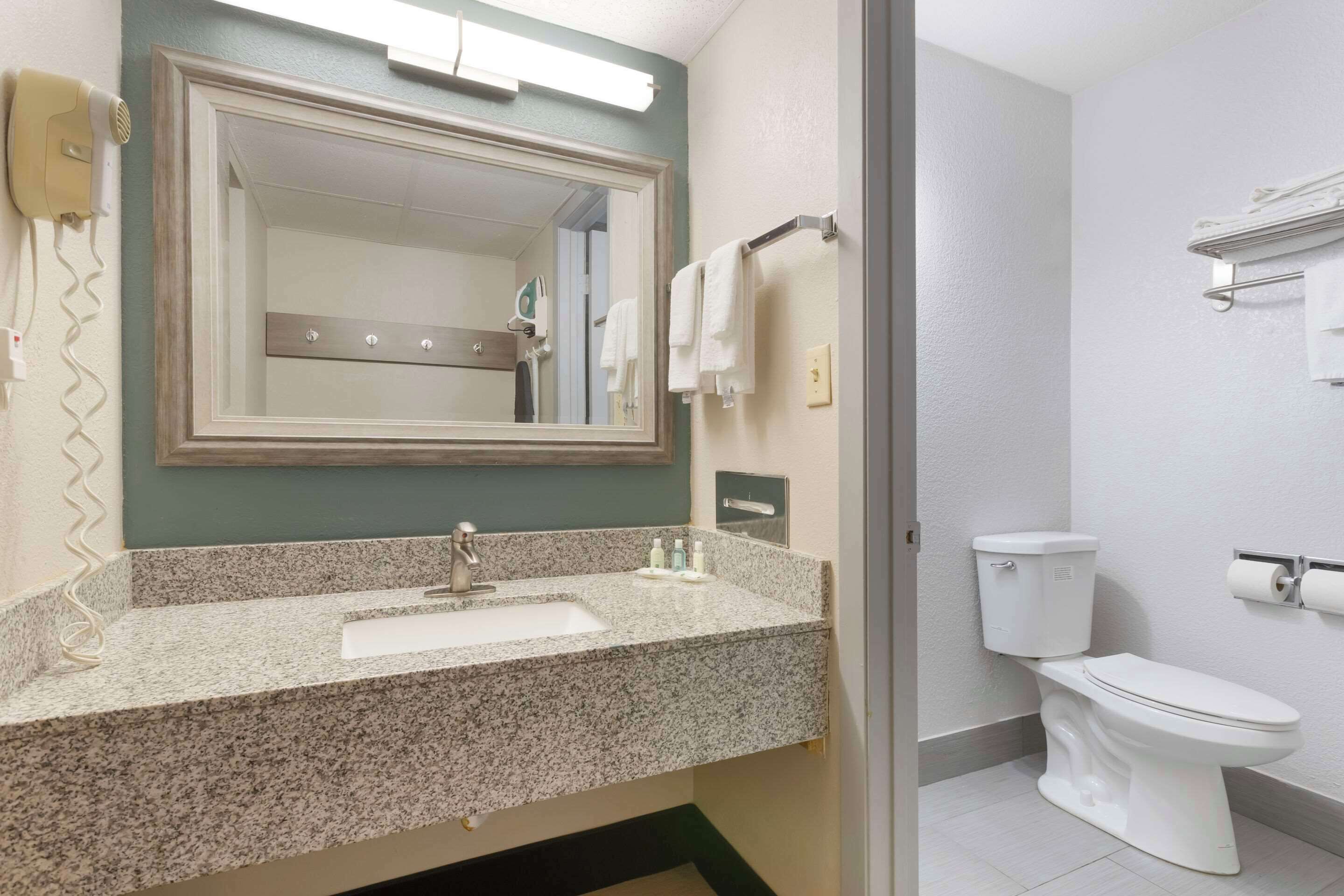 A bathroom with a granite countertop sink, a mirror, a toilet, and a towel rack.
