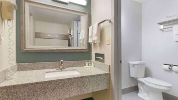 A bathroom with a granite countertop sink, a mirror, a toilet, and a towel rack.