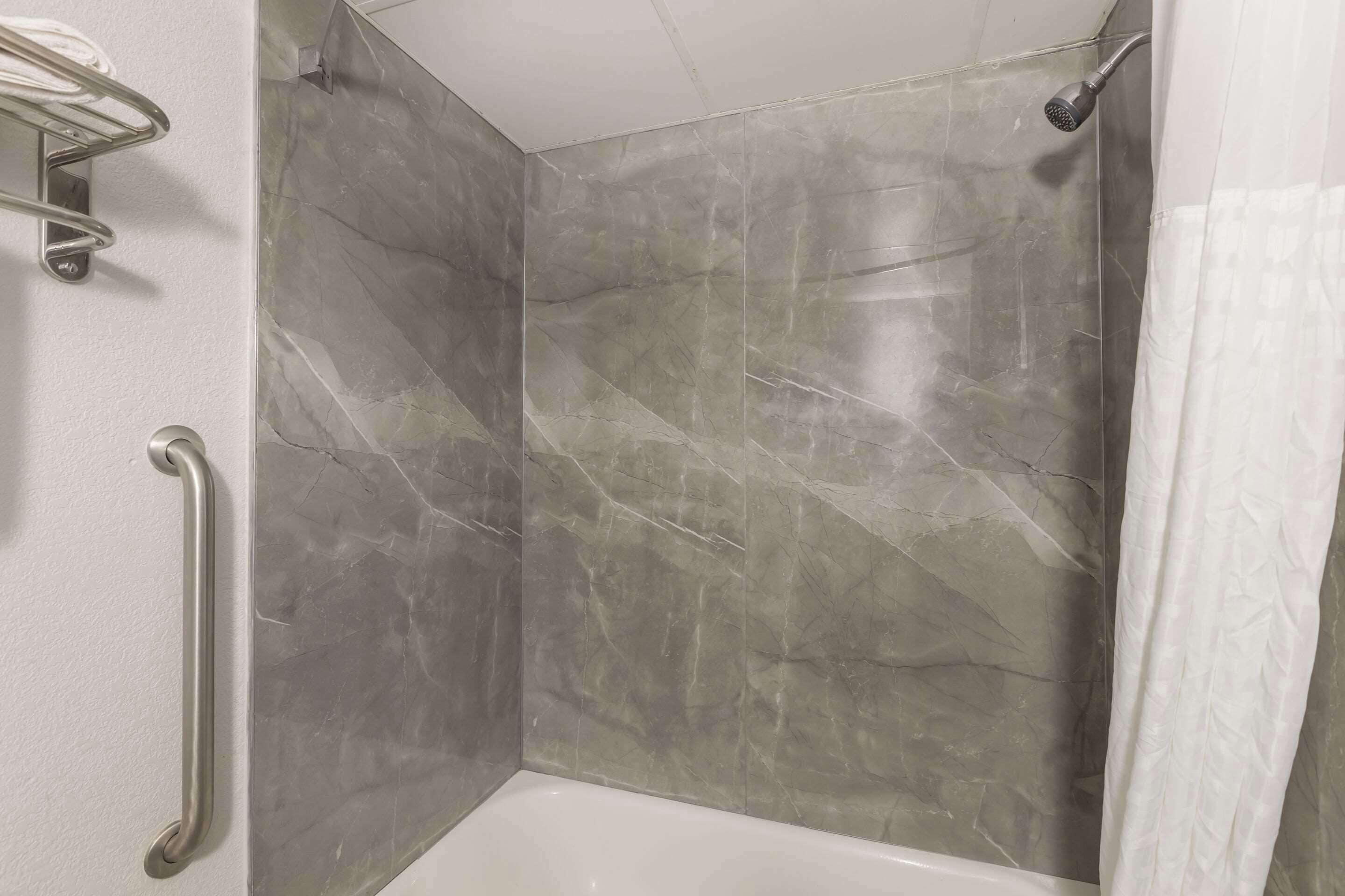 A shower area with a glass door, a handrail, and a showerhead.