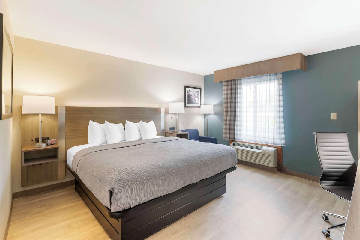 A modern hotel room with a large bed, bedside tables with lamps, a desk, and a chair.