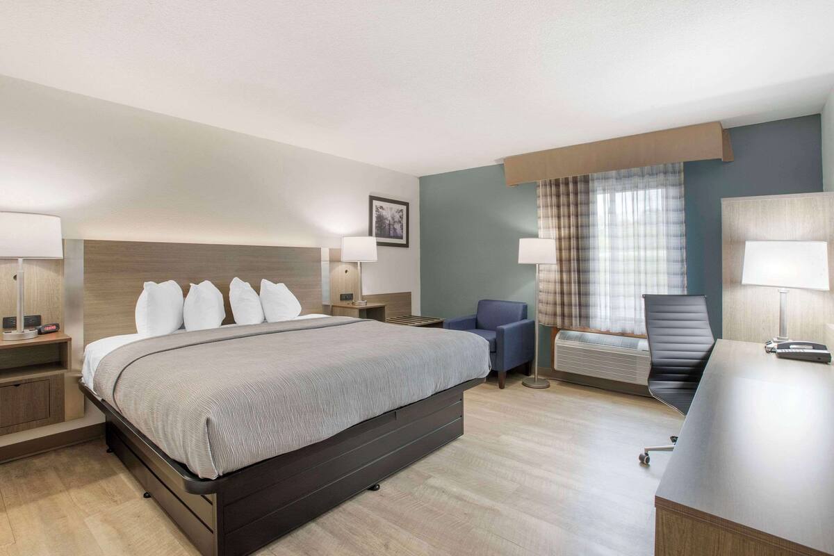 A modern hotel room with a large bed, a desk, a chair, and a window with curtains.
