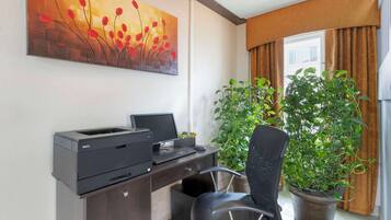 A hotel room with a desk, printer, chair, and two potted plants.