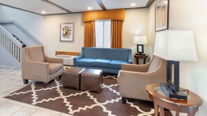 Een moderne woonkamer met een blauwe bank, beige fauteuils, een kamerkleed met patroon en een trap aan de linkerkant.