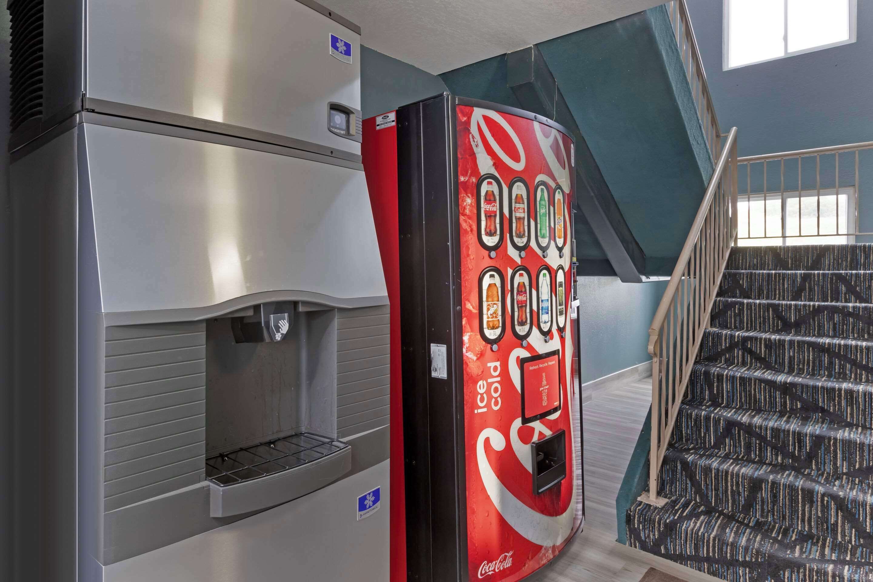 A vending machine with a Coca-Cola logo, a stainless steel appliance, and a staircase with patterned carpet.