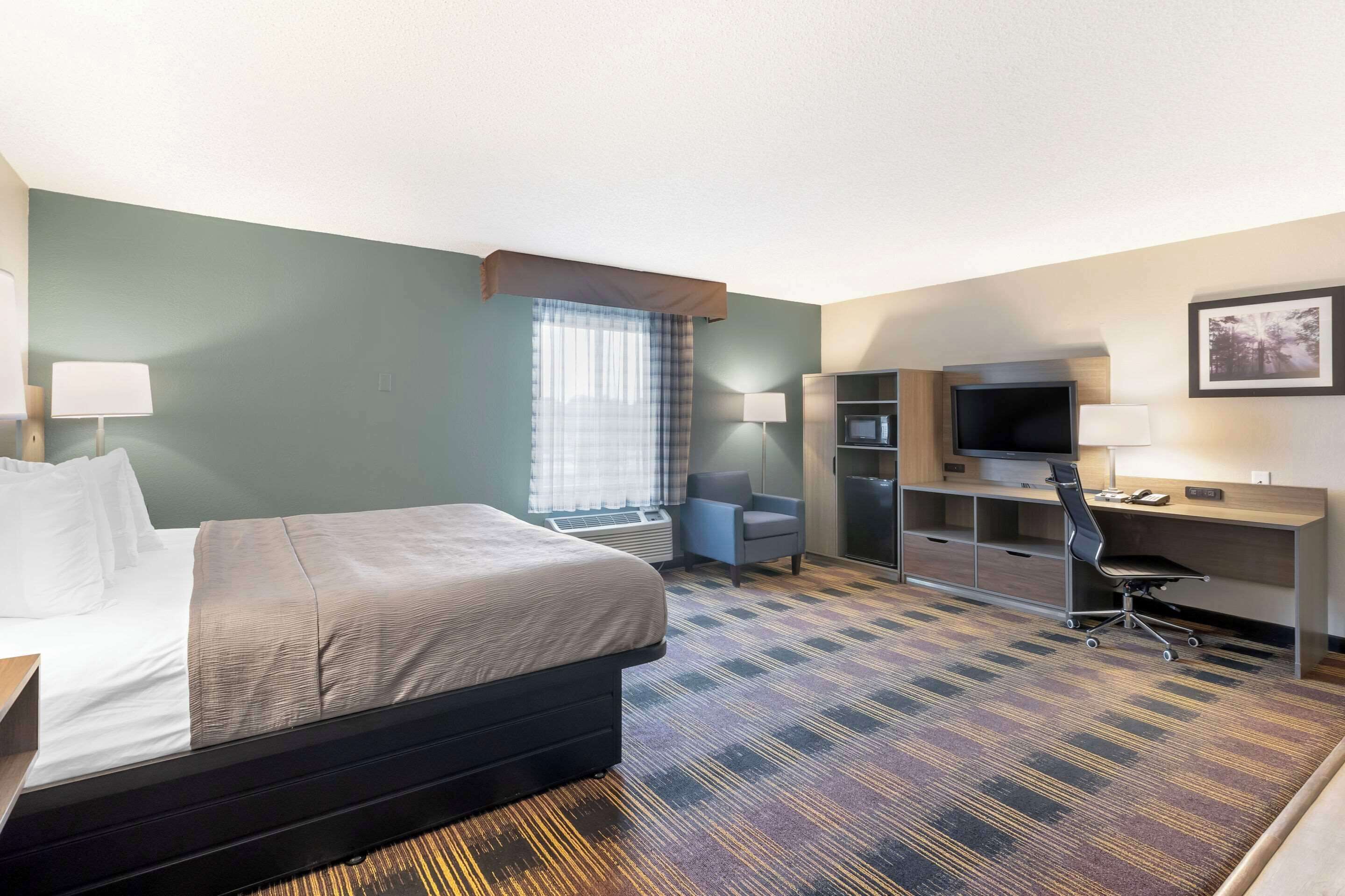 Habitación de hotel con cama, escritorio, silla, televisión y ventana con cortinas.