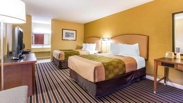 Habitación de hotel con dos camas, un escritorio, televisión y ventana con cortinas.
