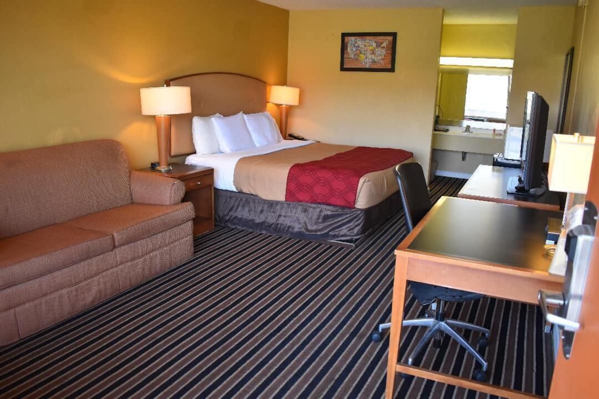 Una habitación de hotel con cama, escritorio, silla, sofá y televisión.