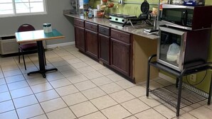 Una cocina con suelo de baldosas, ventana, mesa y microondas.