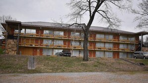 Un motel de varios pisos con fachada de piedra, varios balcones y un camino de acceso de grava.