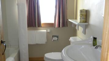 A bathroom with a toilet, bidet, and sink. There is a window with curtains, a towel rack, and a toilet paper holder.
