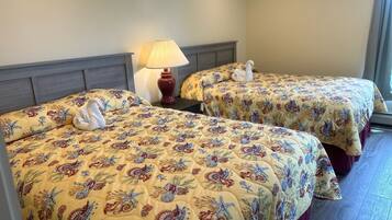 Two beds with floral and sea creature bedding, a nightstand with a lamp, and a window with curtains.