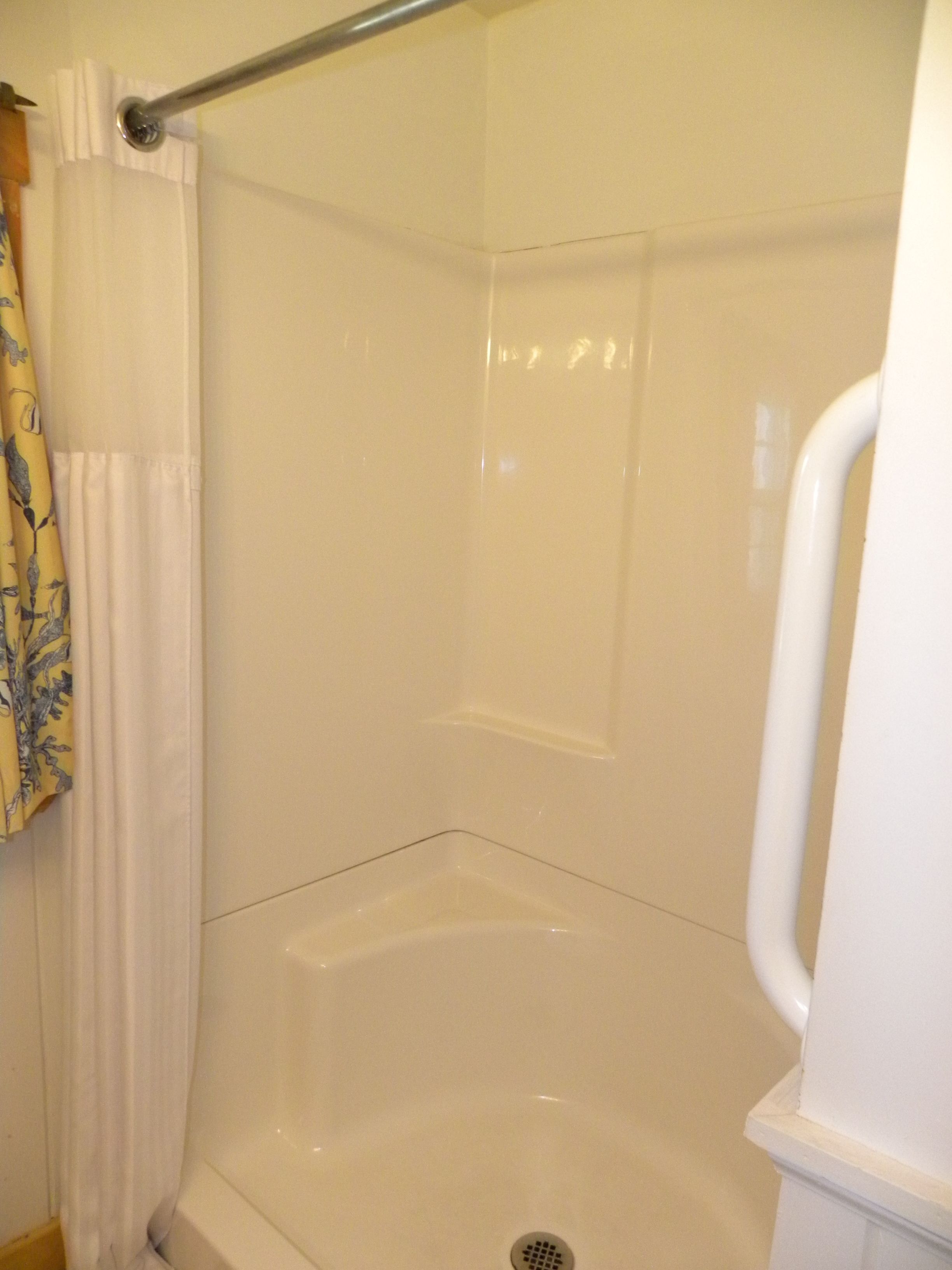 A shower stall with a white curtain and a metal grab bar.
