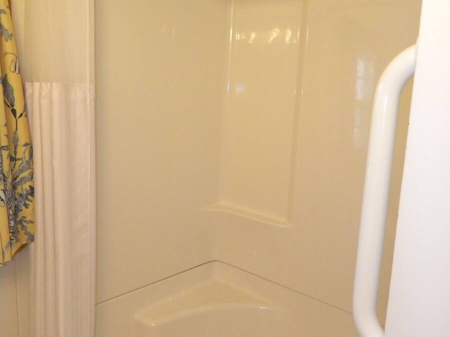 A shower stall with a white curtain and a metal grab bar.