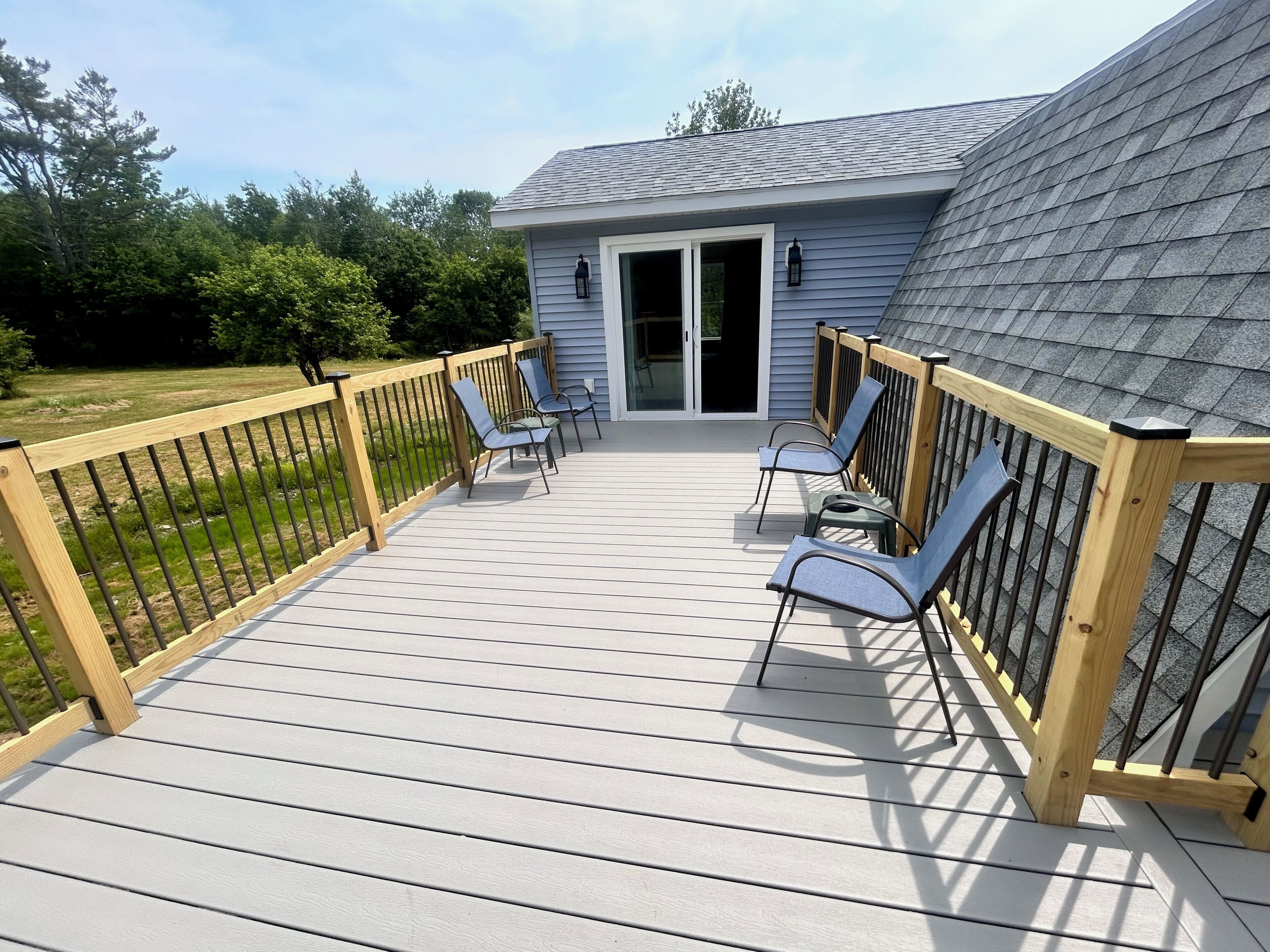 A deck with a wooden railing, a small building with a door, and two chairs.