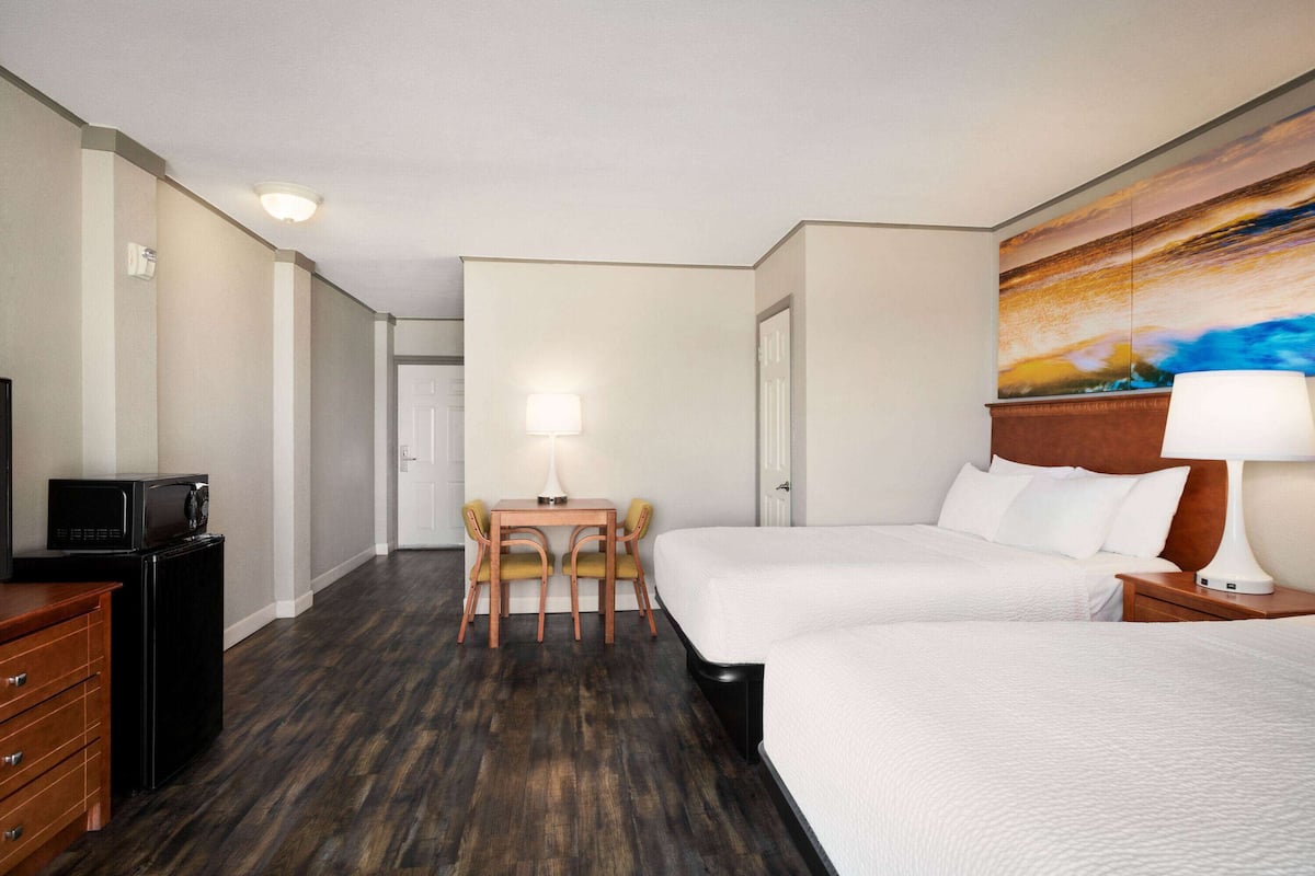 A hotel room with two beds, a desk with chairs, a microwave, and a painting on the wall.