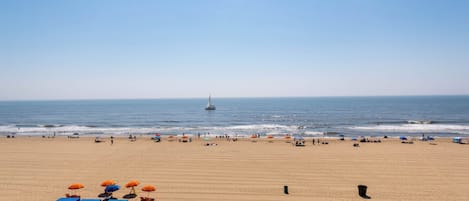 A beach with umbrellas and a sailboat in the distance.