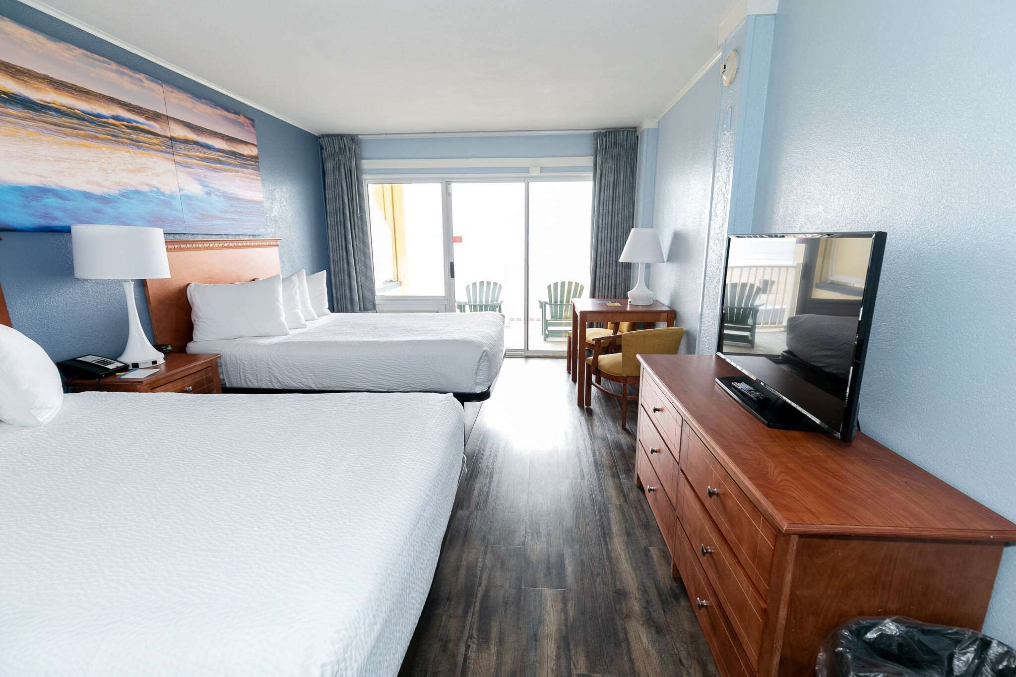 A hotel room with two beds, a wooden dresser, a television, and a painting on the wall.