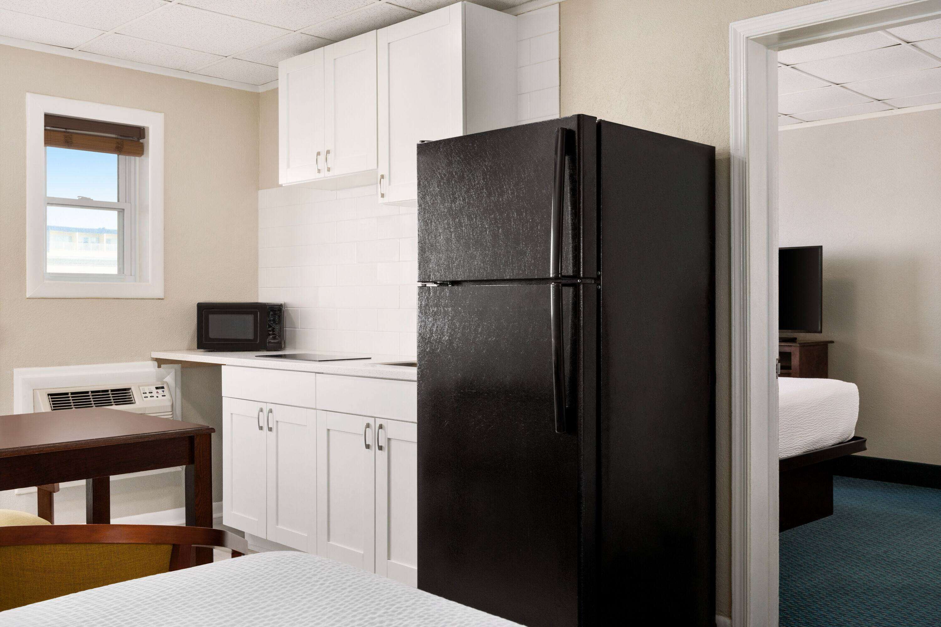 Une chambre d’hôtel compacte comprenant un coin cuisine, un réfrigérateur noir, un four à micro-ondes, une petite table et un lit.