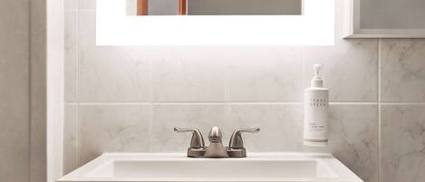 A bathroom with a white sink, a mirror above it, and a bottle of hand soap on the counter.