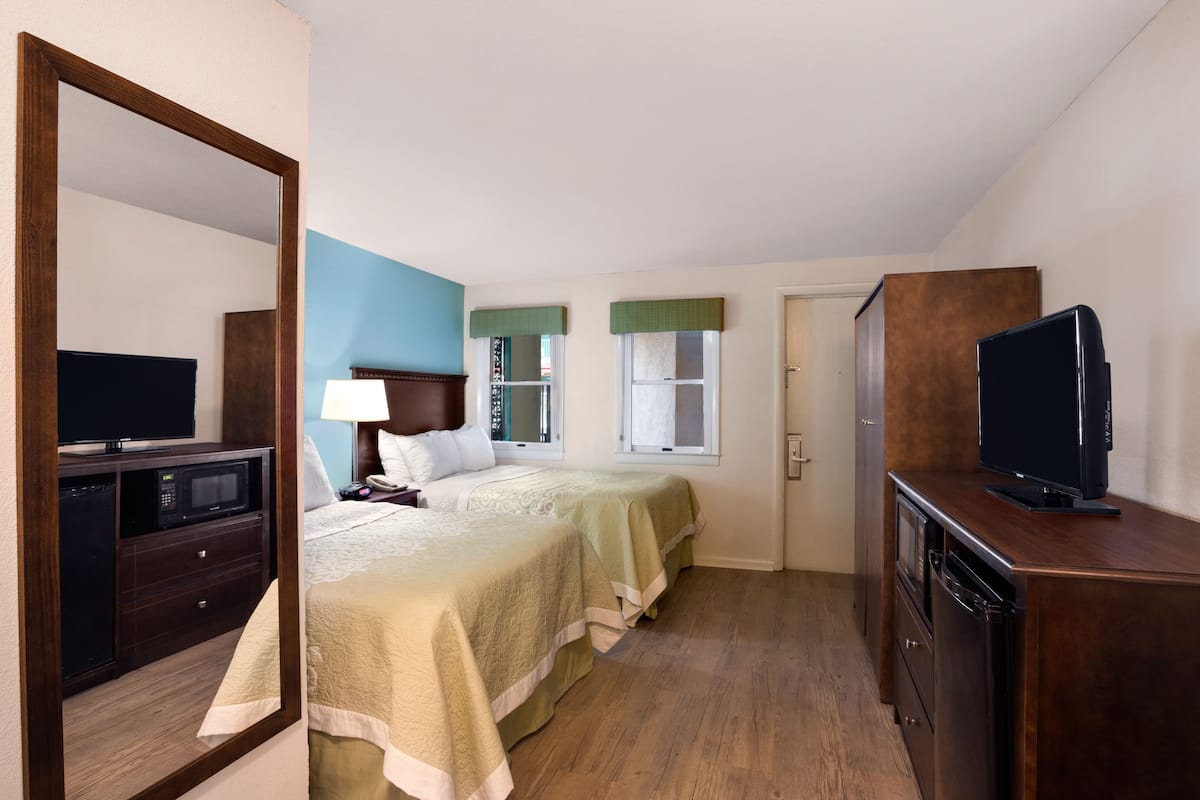 A hotel room with a bed, bedside table, lamp, TV, and a microwave.