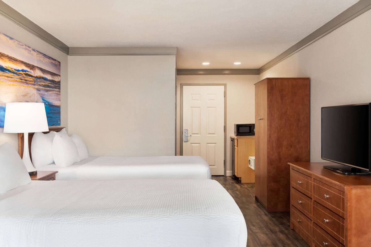A hotel room with two beds, a TV, a wooden dresser, and a painting on the wall.