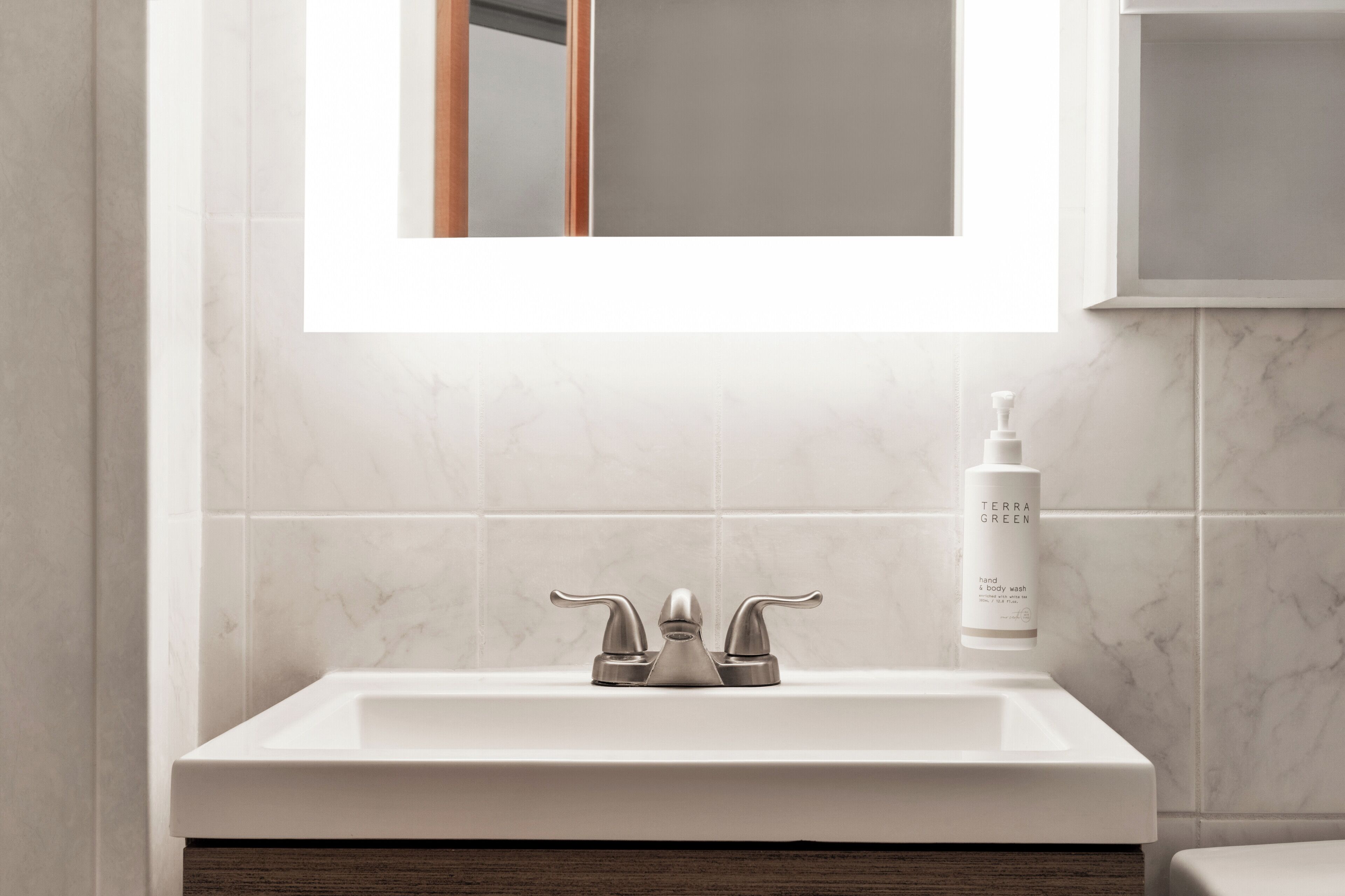 A bathroom with a white sink, a mirror, and a bottle of hand soap.