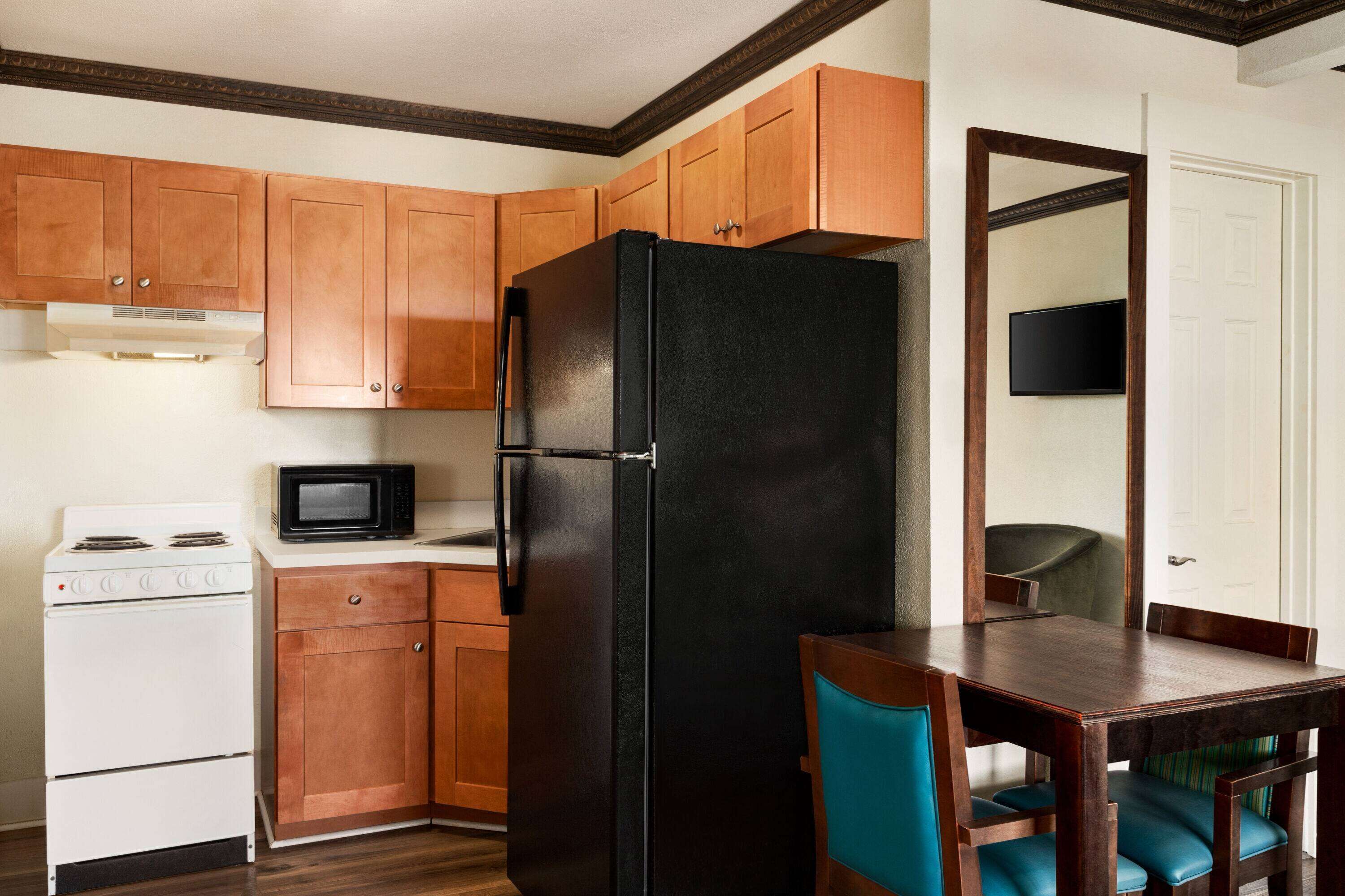 Une cuisine avec des meubles de rangement en bois, un réfrigérateur noir, une cuisinière blanche et un four à micro-ondes.